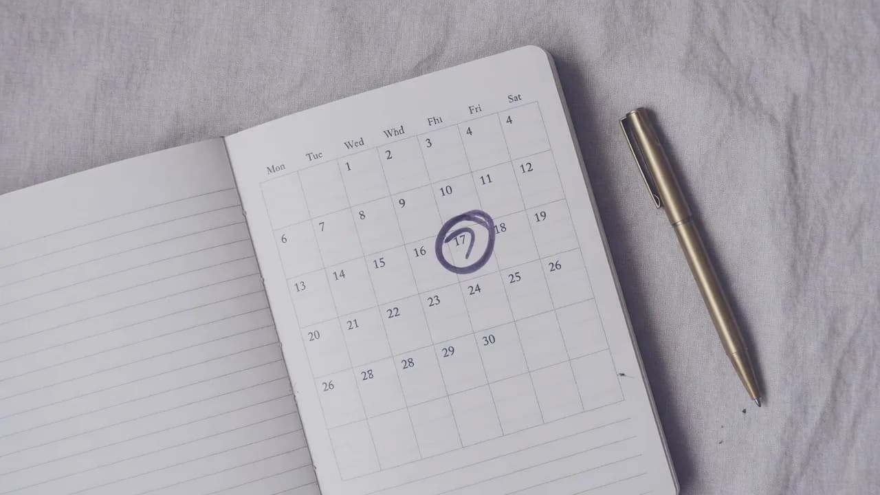 Open notebook calendar with a single date circled and a brass pen on linen